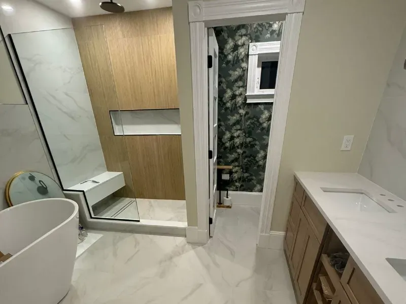 Master bathroom with large-format Calacatta porcelain floor tile, wood-look shower accent wall, freestanding tub, and frameless glass door by CLA New England Tile – Boston MA
