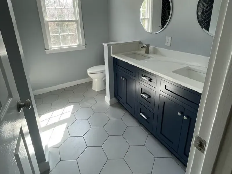 Bathroom remodel featuring oversized white hexagon floor tile, navy blue double vanity, and herringbone tile shower accent by CLA New England Tile – Massachusetts