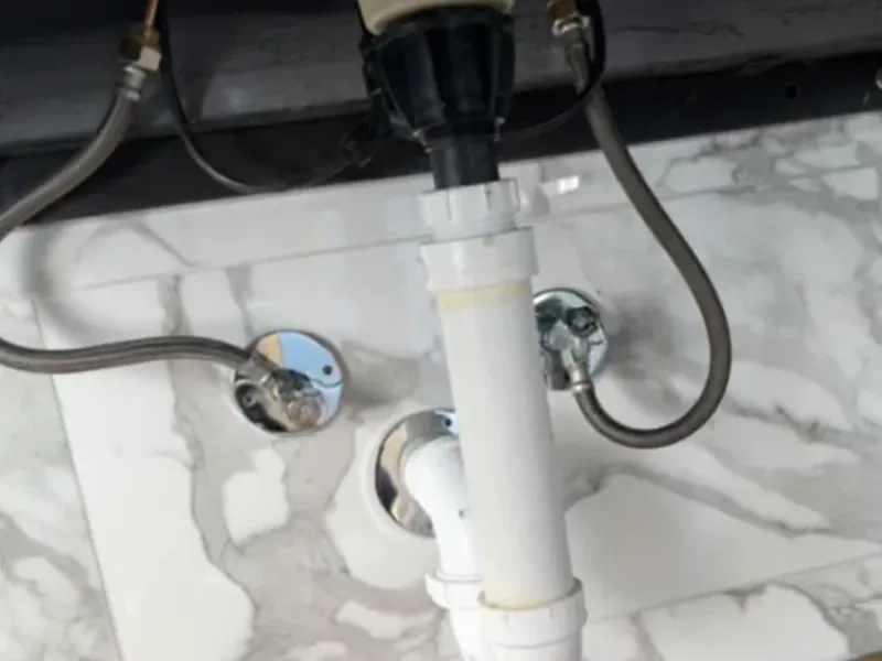 Bathroom plumbing rough-in under vanity with drain, supply lines and water connections on marble tile floor by CLA New England Tile – Boston MA