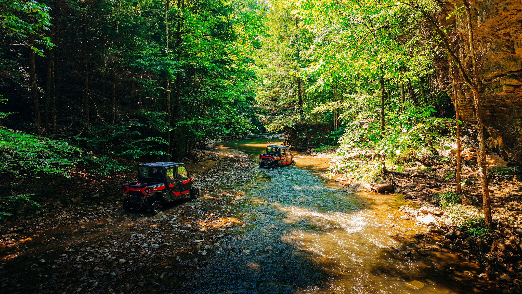Two side-by-sides crossing a creek in the Red River Gorge forest