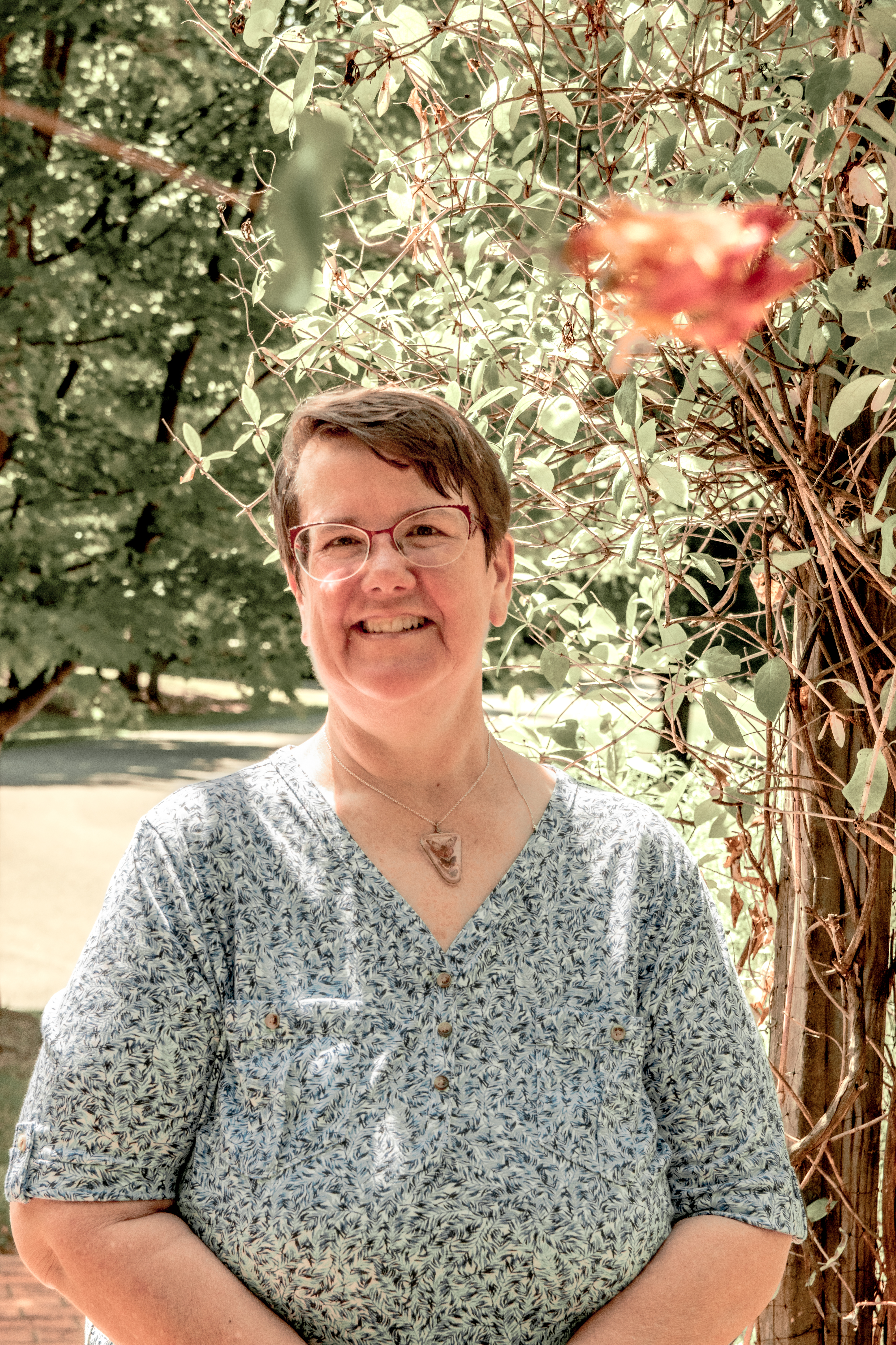 A picture of the Quest Creator. She is standing under an arbor smiling in the sun.