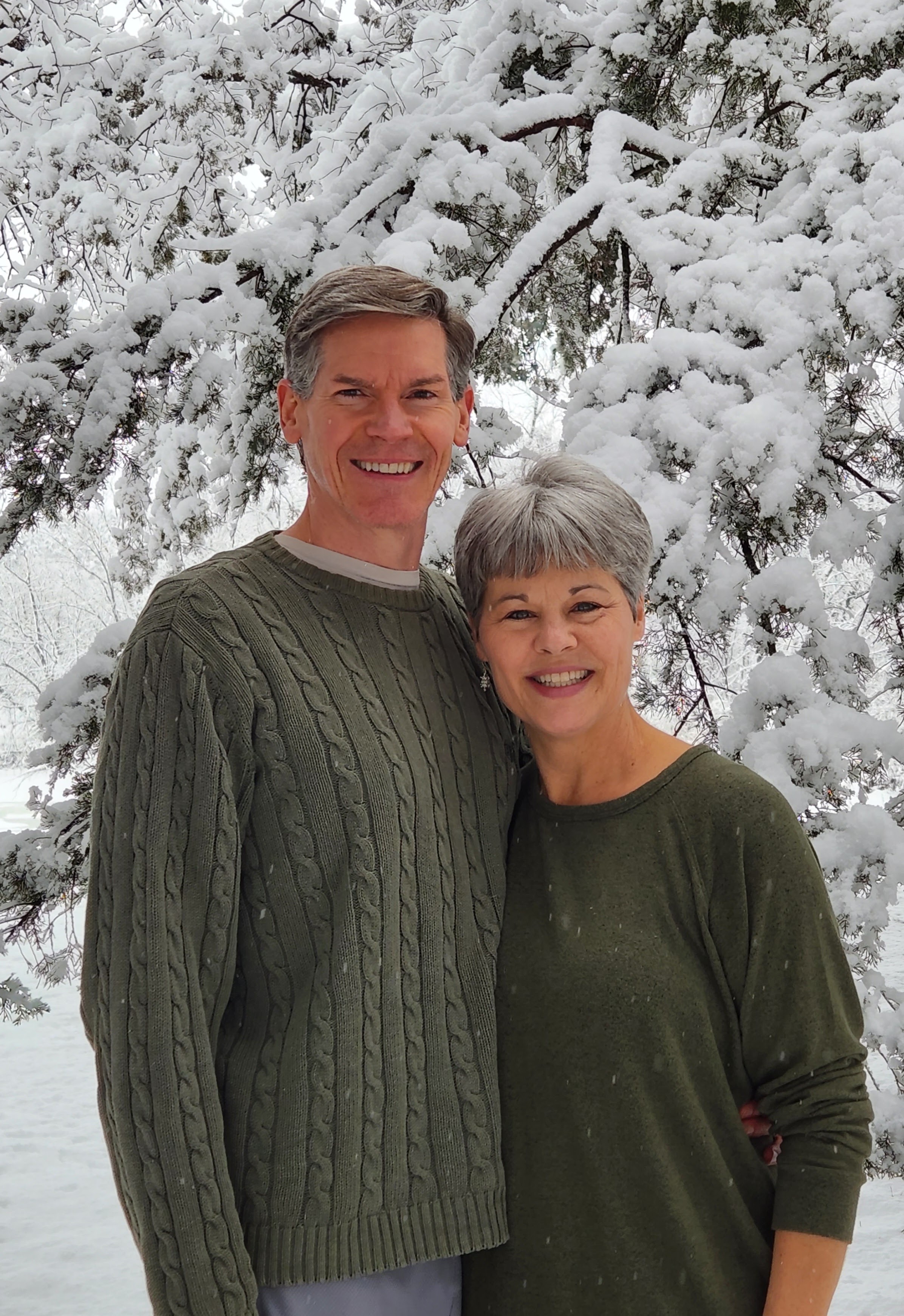 Jim and Maureen Otremba, a smiling couple in their 50s, standing together in a sunlit library filled with spiritual books, exuding warmth, wisdom, and approachability.