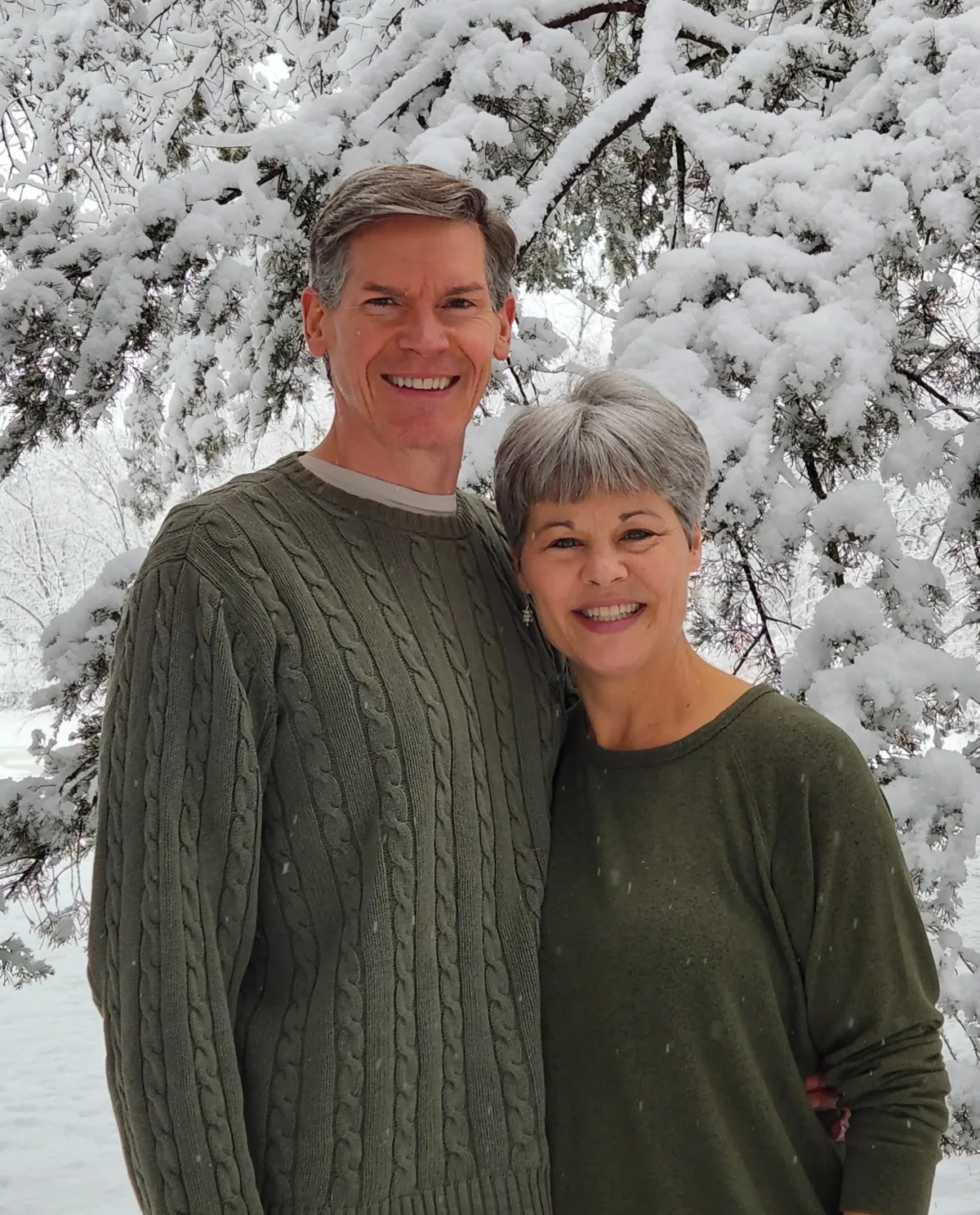 Jim and Maureen Otremba, a smiling couple in their 50s, standing together in a sunlit library filled with spiritual books, exuding warmth, wisdom, and approachability.