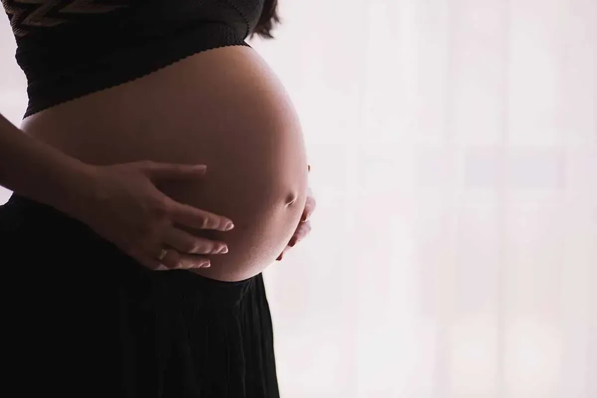 A gentle side-profile shot of a pregnant woman cradling her baby bump, representing prenatal massage, maternal care, and physical wellness.