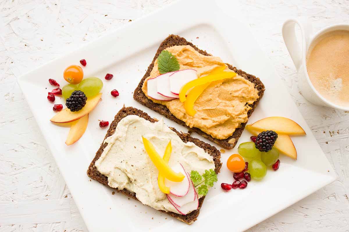 A top-down view of nutritious open-faced breakfast toasts with healthy toppings served on a white plate next to a hot beverage, representing a balanced diet.