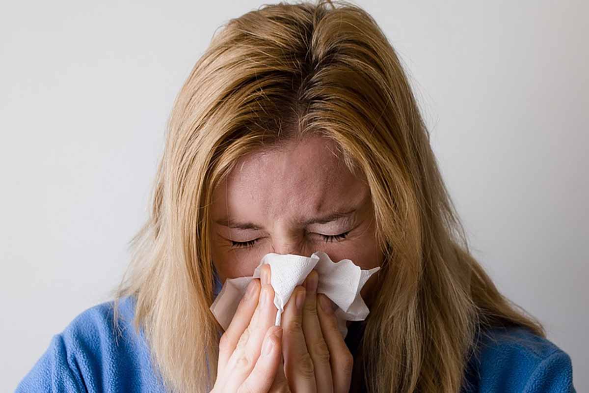 A close-up shot of a young woman suffering from allergy symptoms and sneezing into a tissue, illustrating the need for immunotherapy or allergy shots.