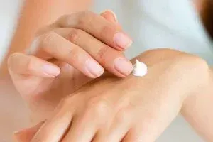 A close-up shot of a person applying a small dollop of white moisturizing cream onto their hand, illustrating natural skincare and naturopathic treatments for eczema relief.