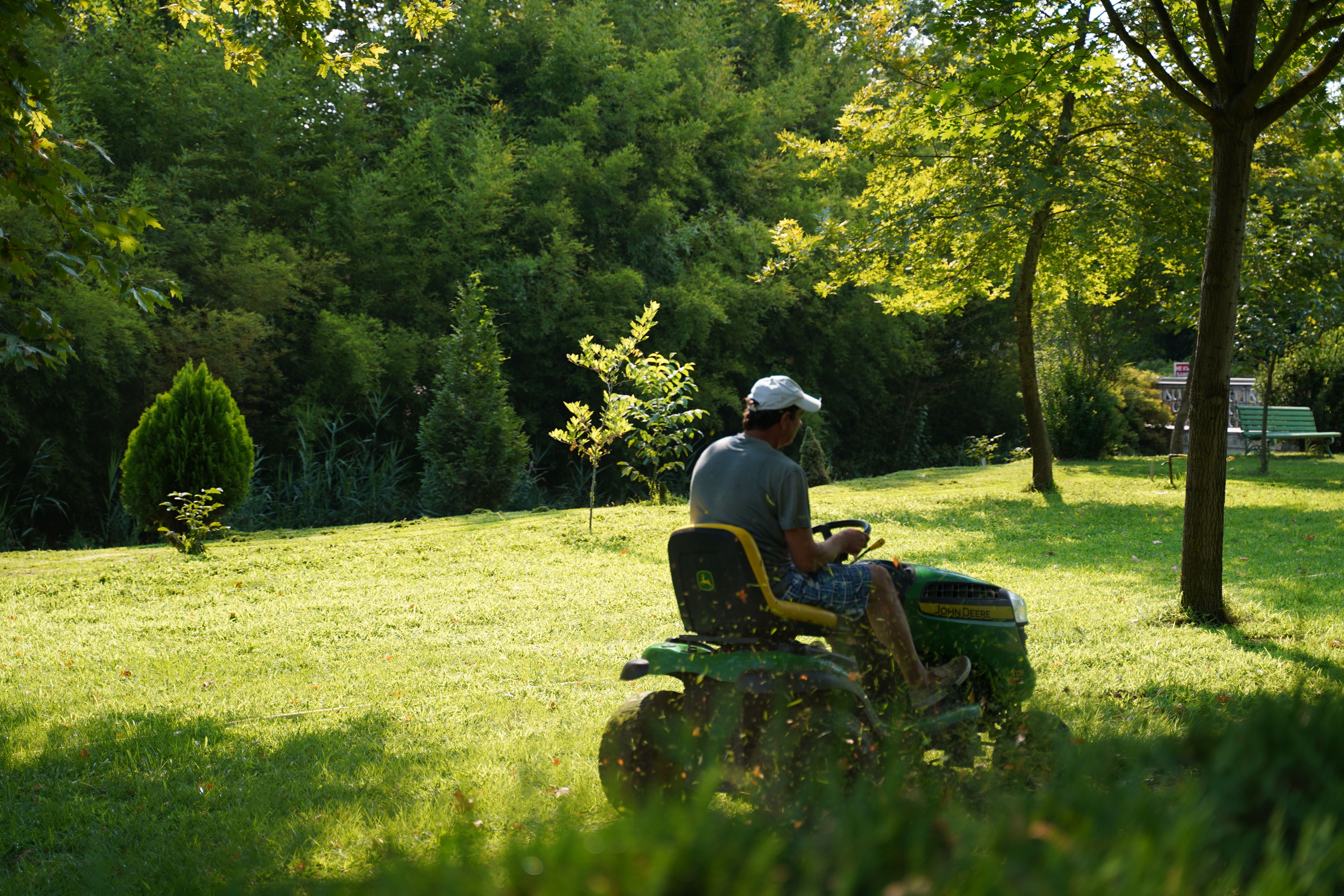 Jardinero profesional cortando césped con tractor cortacésped en jardín arbolado - Jardinería y Paisajismo JS