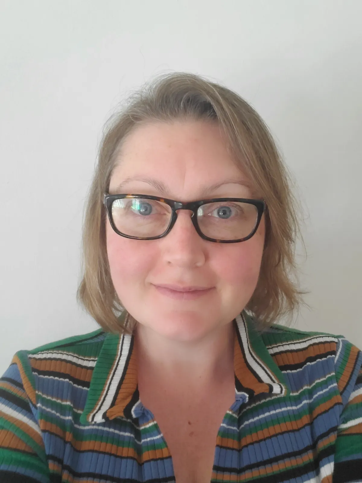 Beth Upton head shot. She wears a stripy top and dark drimmed spectacles and looks plainly at the camera