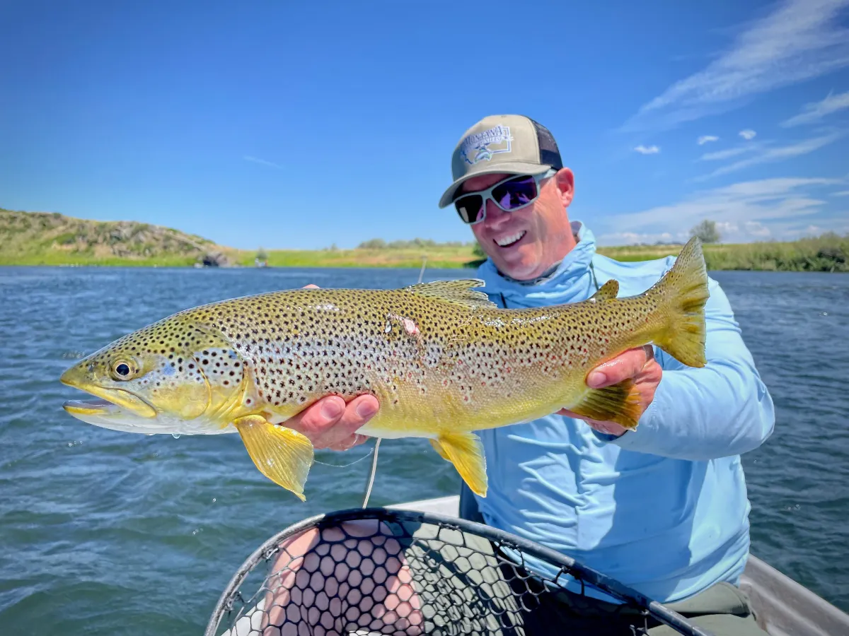 Darrel DeLeon celebrating on his drift boat while holding two large trout during an epic fly fishing day on Montana’s Missouri River