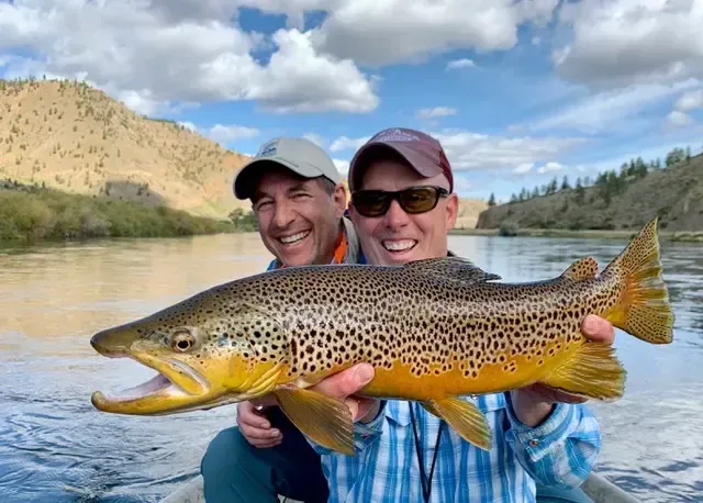 Two smiling men hold a brown trout during a fly-fishing trip on the Missouri River in Montana.