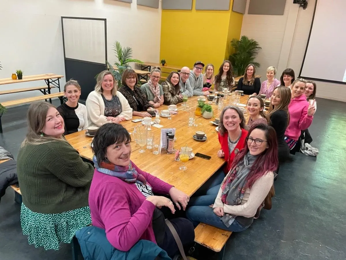 Large group of women sitting around a large table with coffee cups