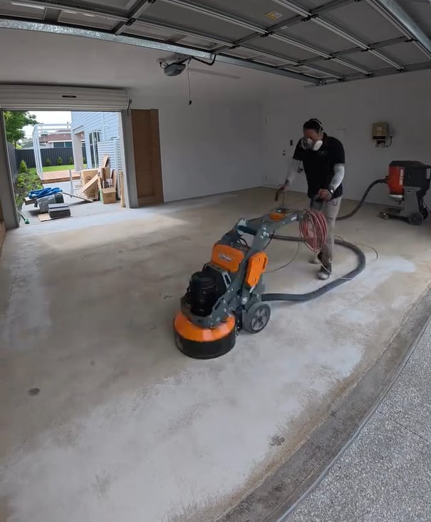 man using an orange concrete grinder to grind and clean up concrete garage floor