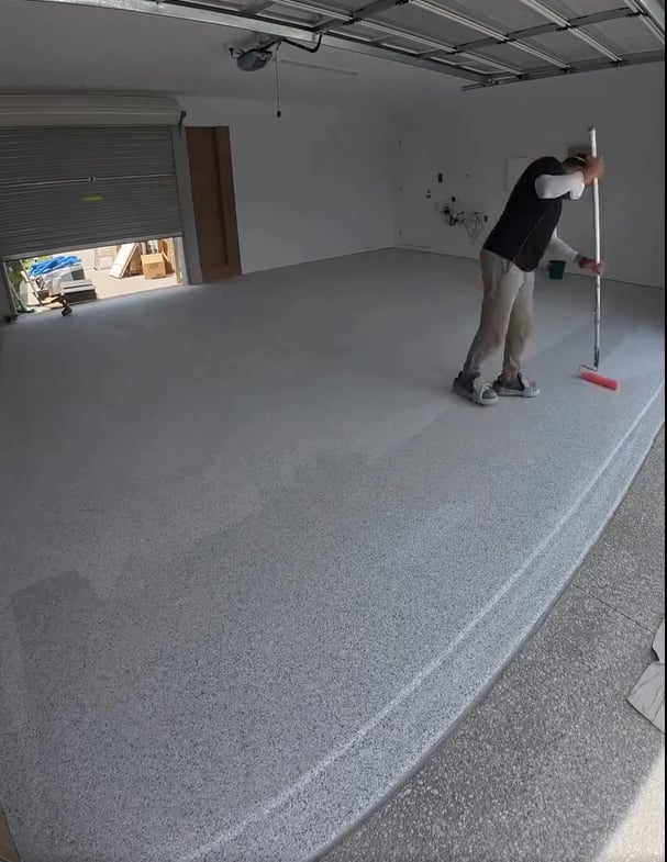 black shirt man using roller to paint epoxy floor