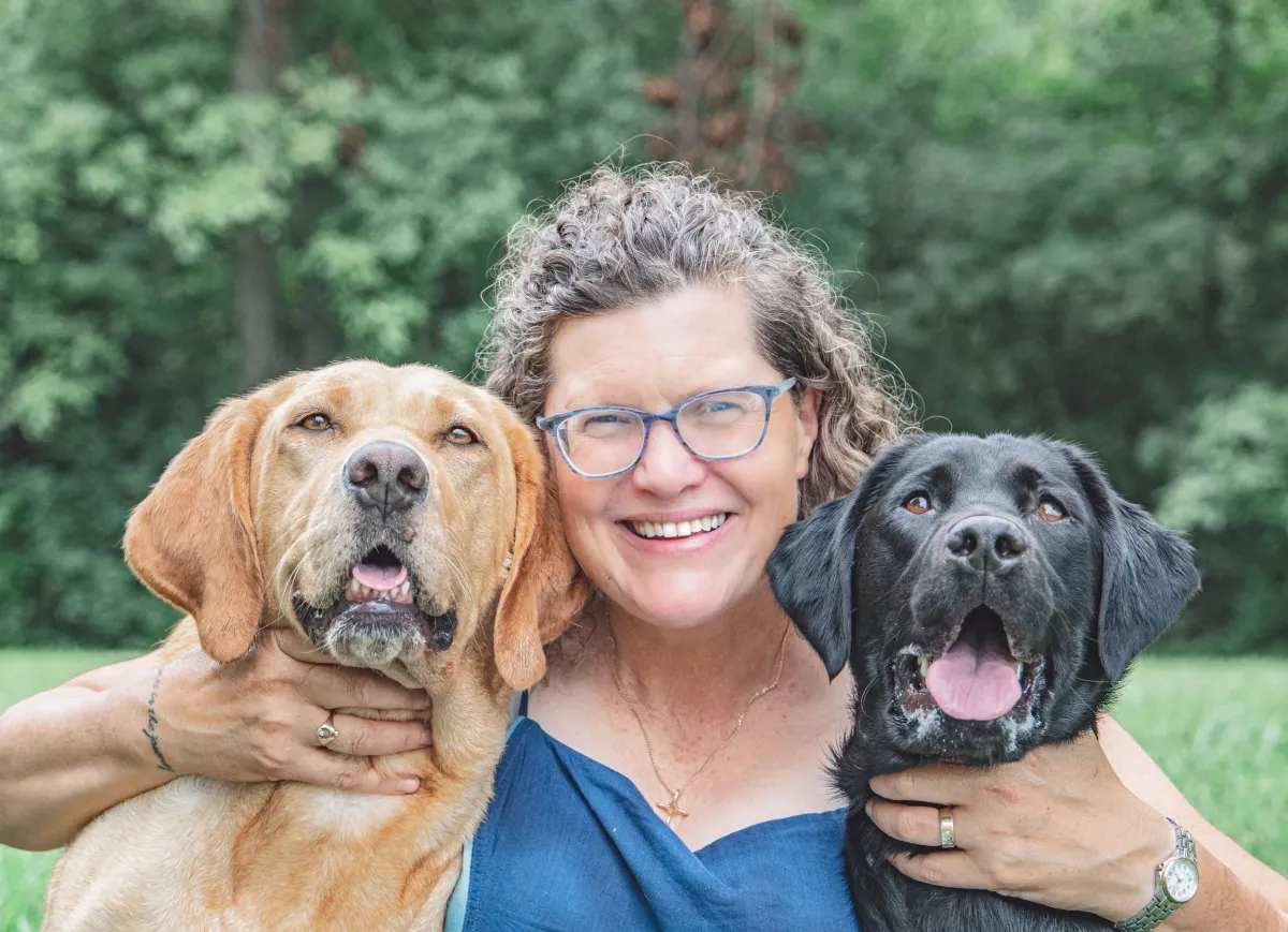 Woman sitting in a field with two dogs
