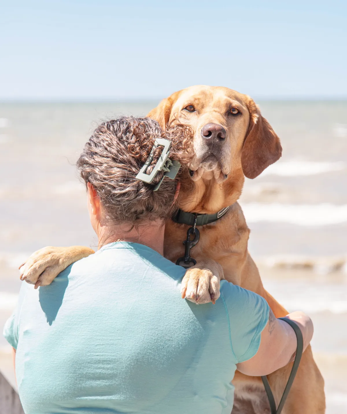 Woman warmly smiling and hugging her golden retriever dog outdoors