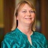 Founder portrait of Dr. Deborah Moerland in a bright home-office setting, confident seated pose, natural light, laptop and a plant visible, conveys educator and entrepreneur persona.
