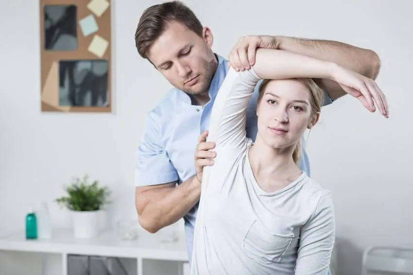 Physiotherapist assisting a woman with shoulder mobility exercises during treatment.