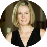 Professional headshot of a smiling blonde woman in a black top against a blurred background.
