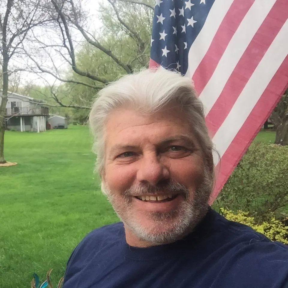 Dale Briggs in a grassy garden with an American flag in the background.