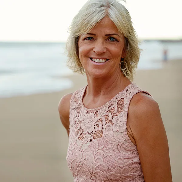 A smiling woman with short blonde hair on a beach