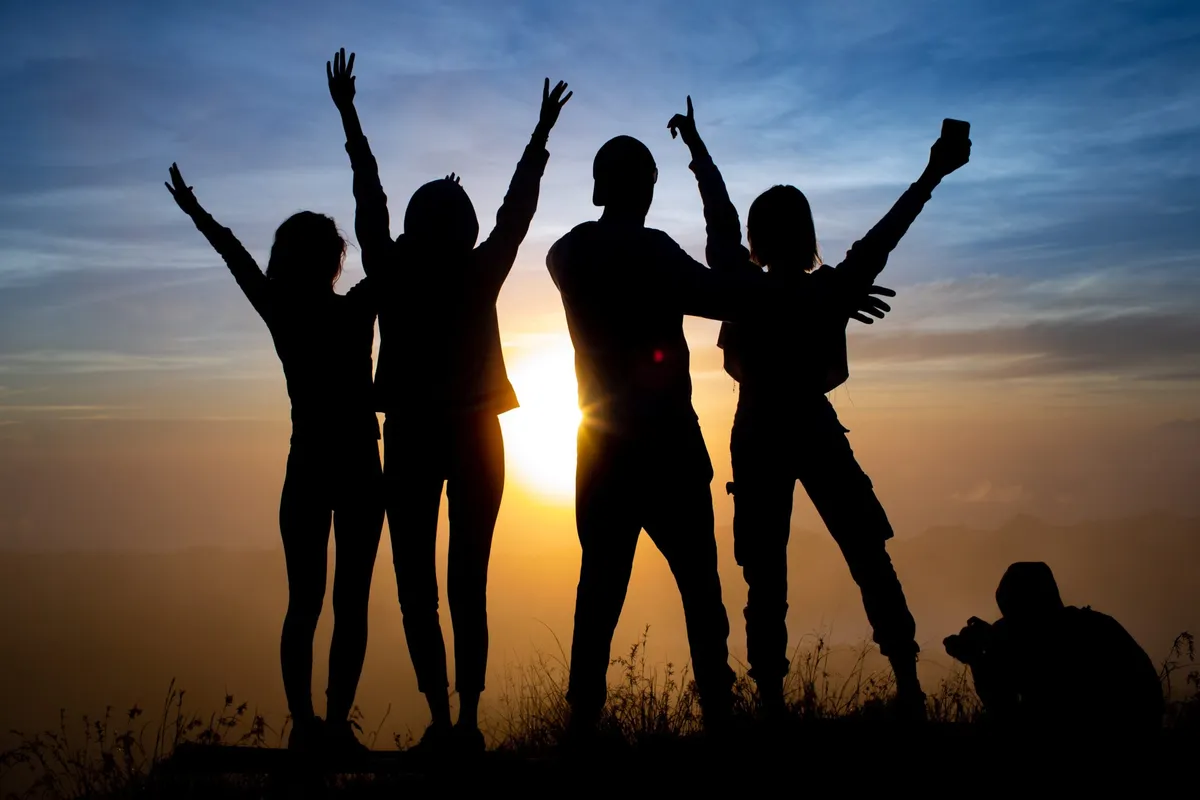 Silhouettes of people raising their arms at sunset