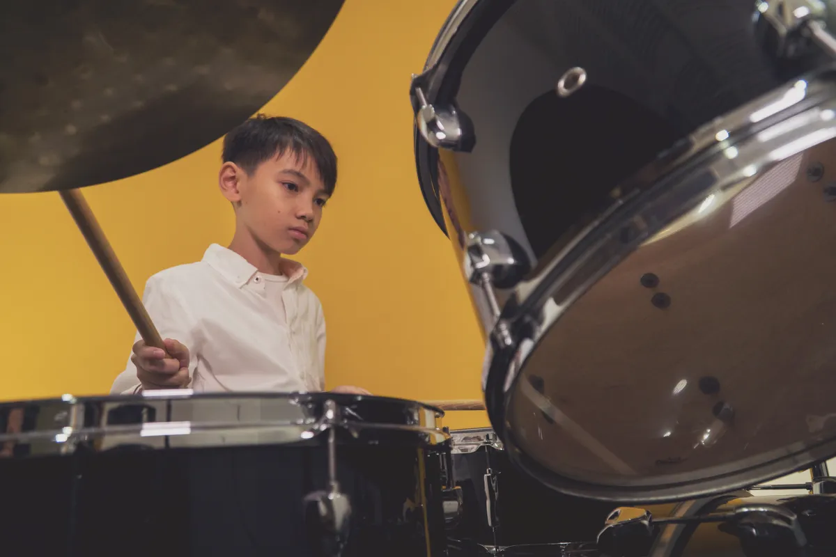 Student playing a drum kit during an individual lesson in a modern music school studio