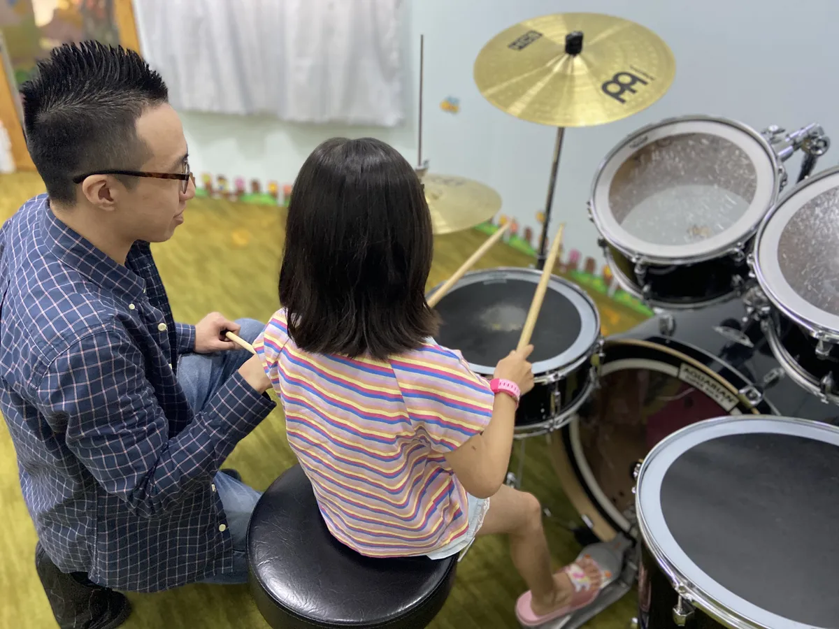 One-to-one drum lesson with a teacher guiding a student at the drum kit