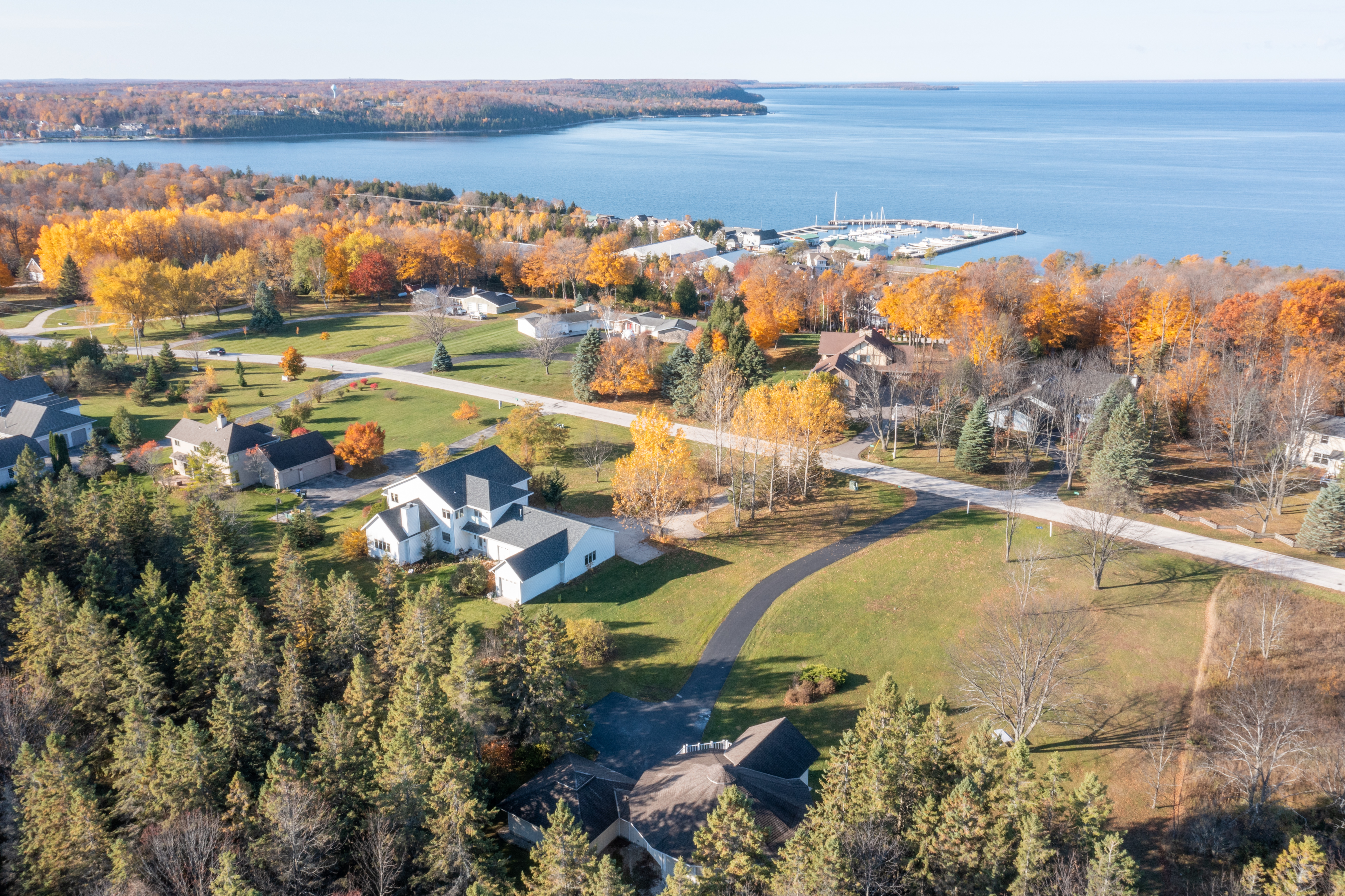 Aerial view of a Door County lakeside home with modern architecture, surrounded by autumn trees, sunlight reflecting on water, and a welcoming porch. The image conveys tranquility, premium care, and local expertise.