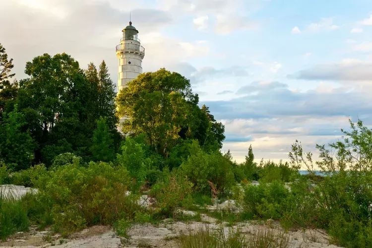 Aerial view of a Door County lakeside home with modern architecture, surrounded by autumn trees, sunlight reflecting on water, and a welcoming porch. The image conveys tranquility, premium care, and local expertise.
