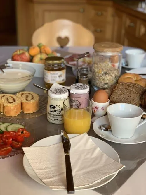 Reich gedeckter Frühstückstisch am Guggenbergerhof in Maria Luggau mit Lesachtaler Brot, frischem Orangensaft, hofeigenen Produkten und Blick in die gemütliche Bauernstube