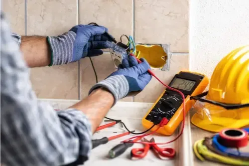 Electrician testing a wall outlet with a circuit tester during a repair call in Southport
