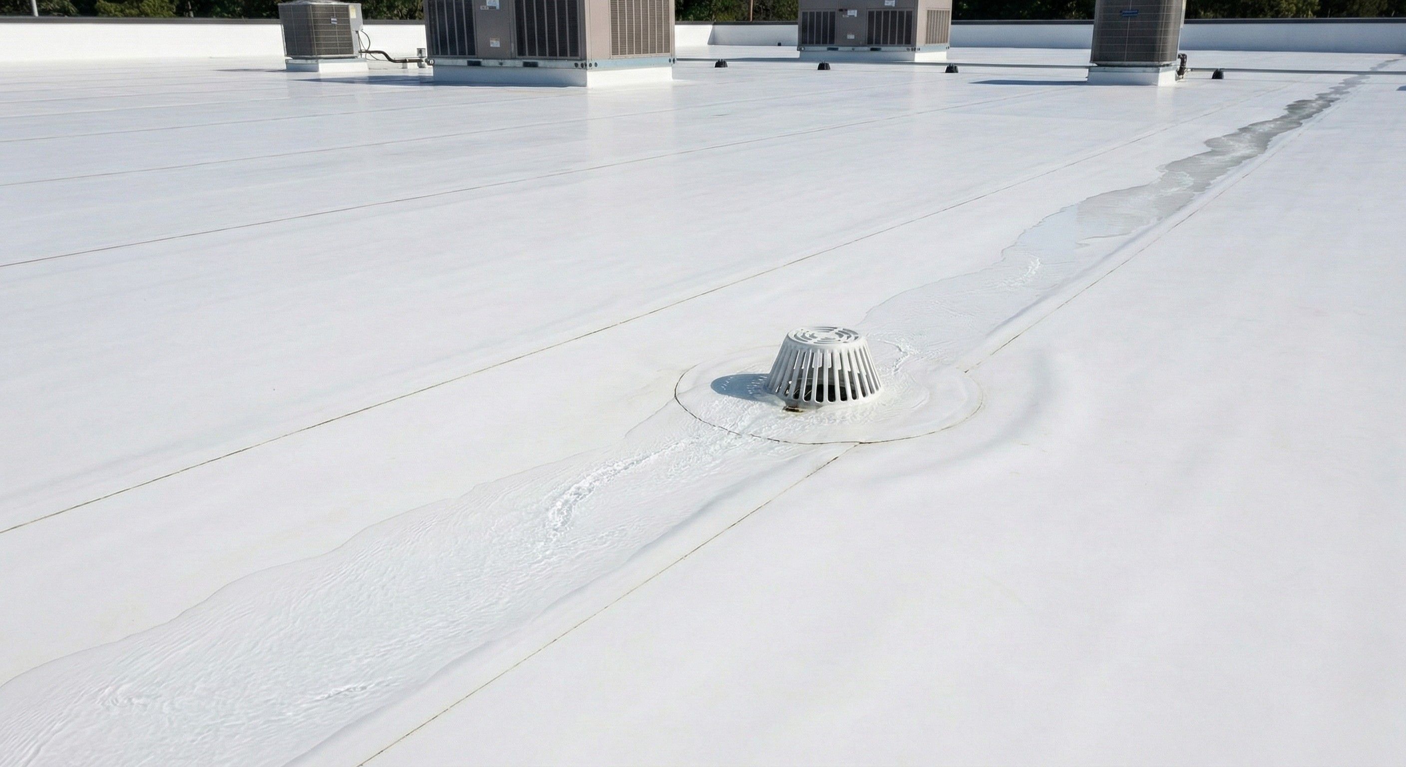 A clean white TPO commercial flat roof installation showing water correctly flowing toward a central roof drain, illustrating precision drainage to prevent ponding.