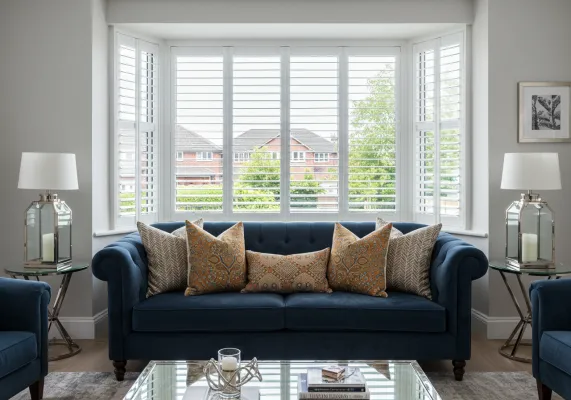 Bay window plantation shutters installed behind a navy living room sofa