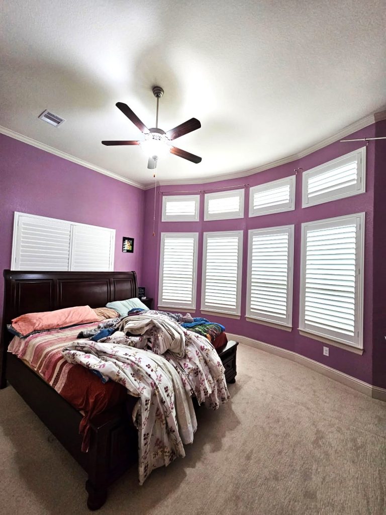 White plantation shutters fitted around a purple bedroom bay window