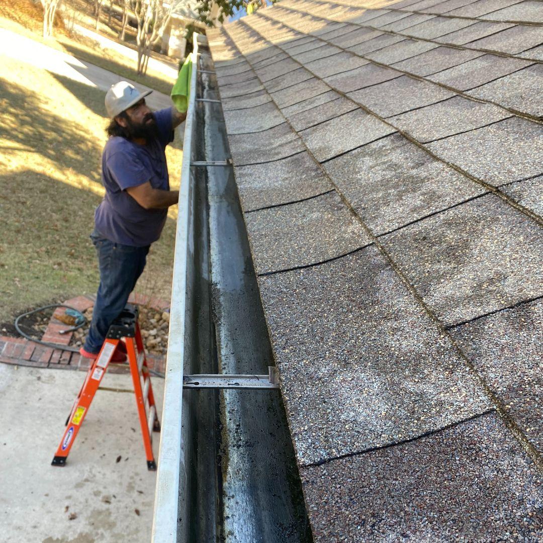 Gutter maintenance and cleaning in San Antonio - worker clearing clogged gutters on residential property to prevent water damage