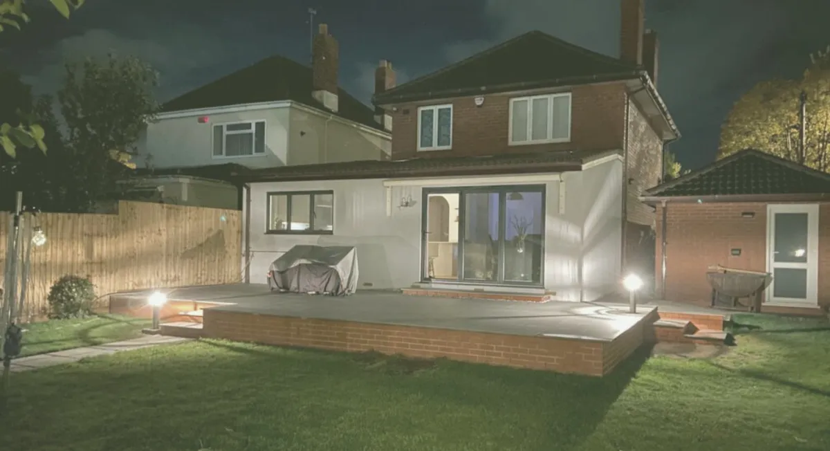 Backyard deck with subtle lighting, large patio area, and a covered grill setup, creating a cozy outdoor gathering space at night.