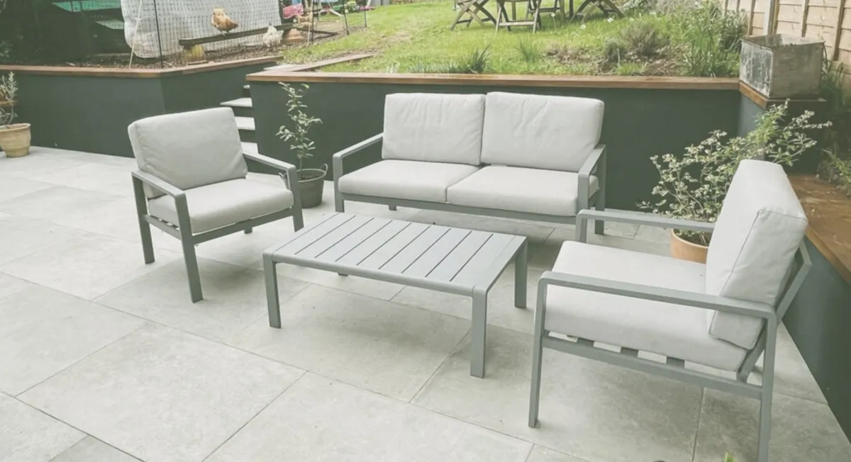 White patio with minimal garden furniture with landscaped back garden.