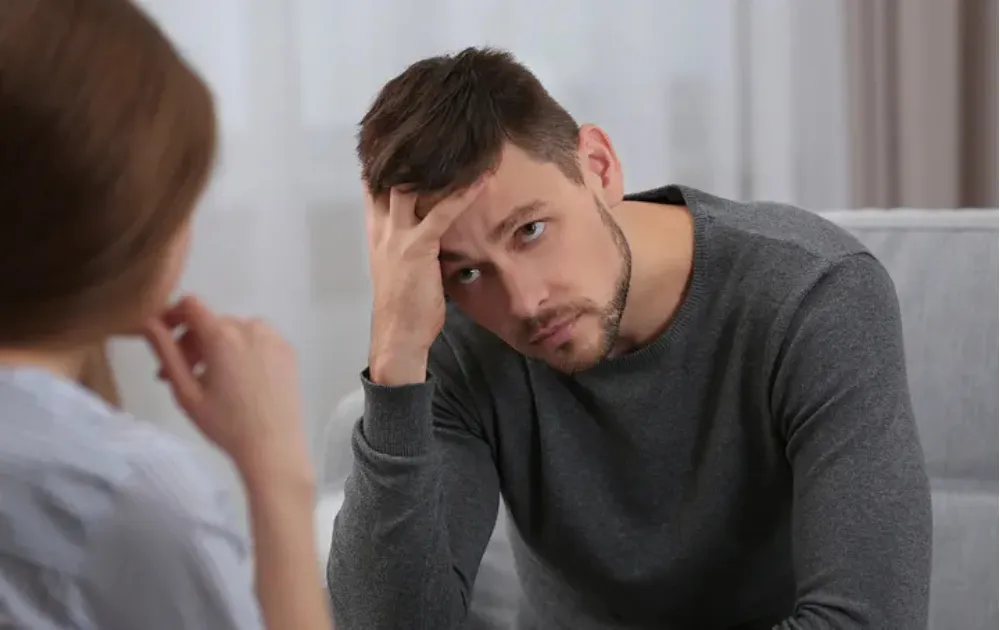 Man with hishead in his hands listening to his wife