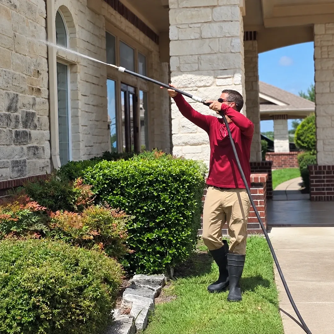 No Pressure SoftWash worker cleaning a stone home exterior