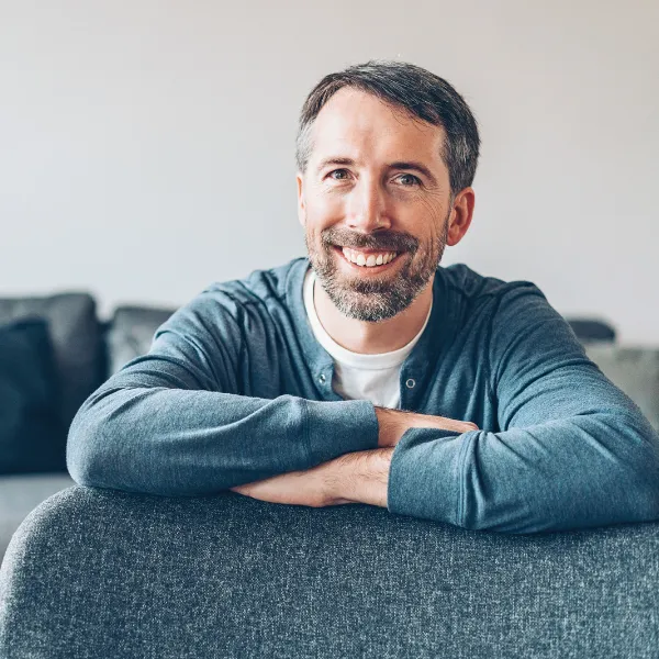 Man smiling and sitting down with arms rested in front of him