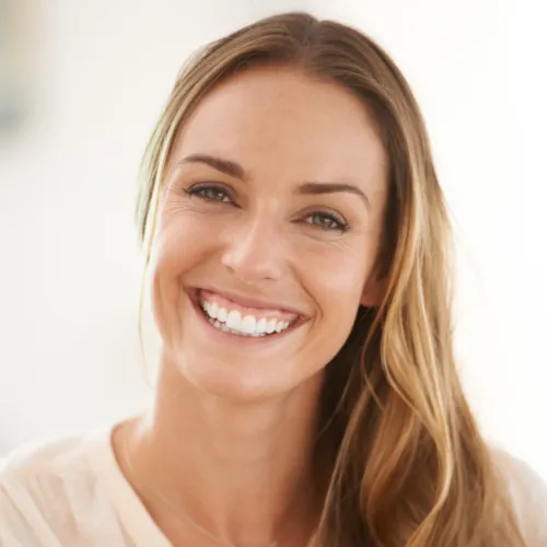 Women in a tan sweater smiling, posing and looking at the camera