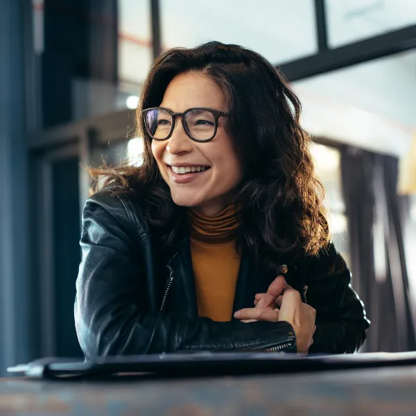 Woman in a black leather jacket, sitting and looking to the side while smiling and having a conversation