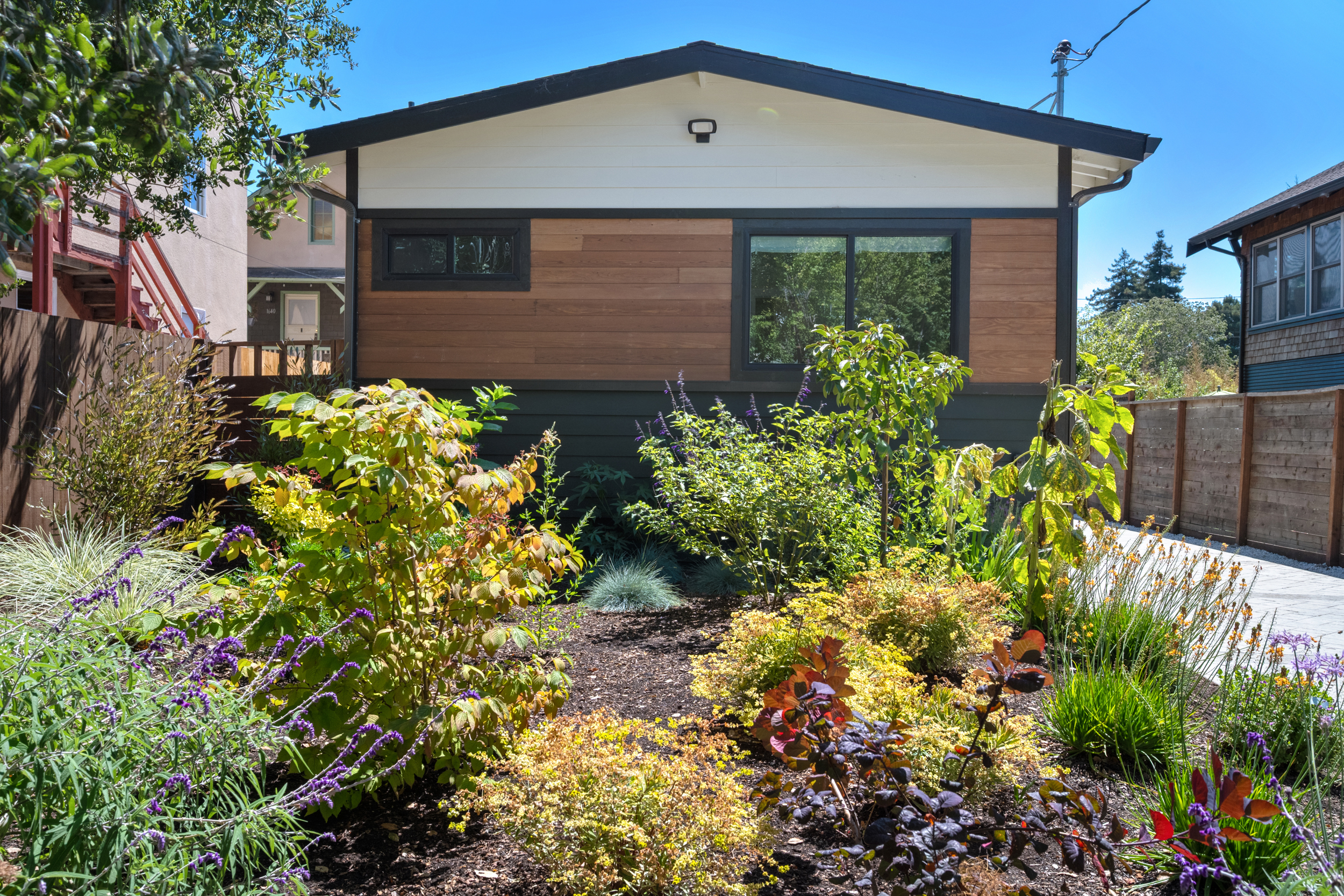 Modern home exterior with horizontal wood siding, black trim, updated windows, and drought tolerant landscaping by Casa de RJ Construction