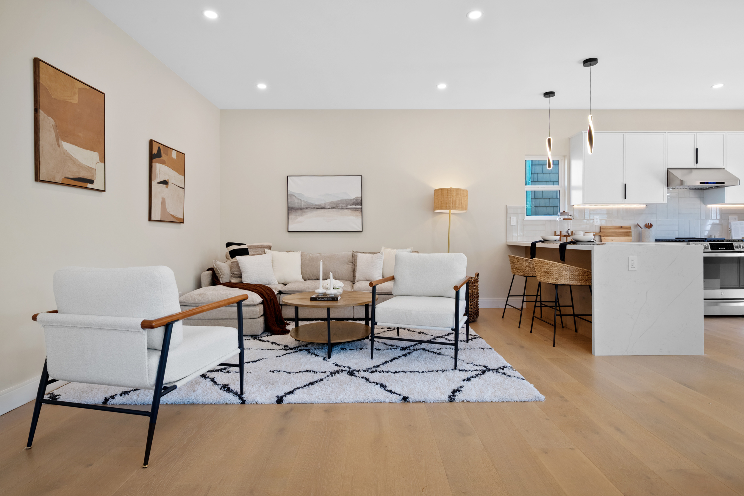 Open concept living room and kitchen with white quartz island, modern lighting, wood flooring, and contemporary furnishings by Casa de RJ Construction