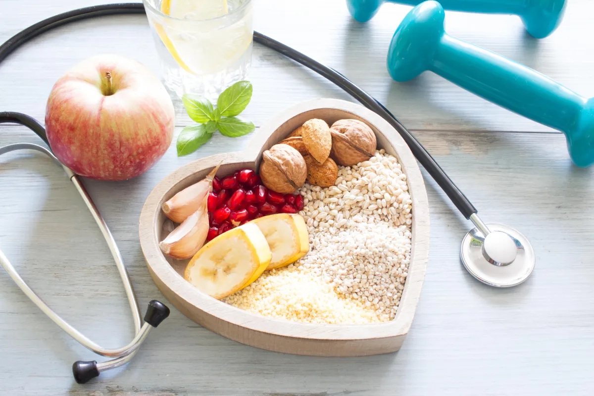 Heart-shaped bowl of fruit with a stethoscope and weights around it, demonstrating how Frosini's Functional Medicine creates a pla leading to overall health for their patients.