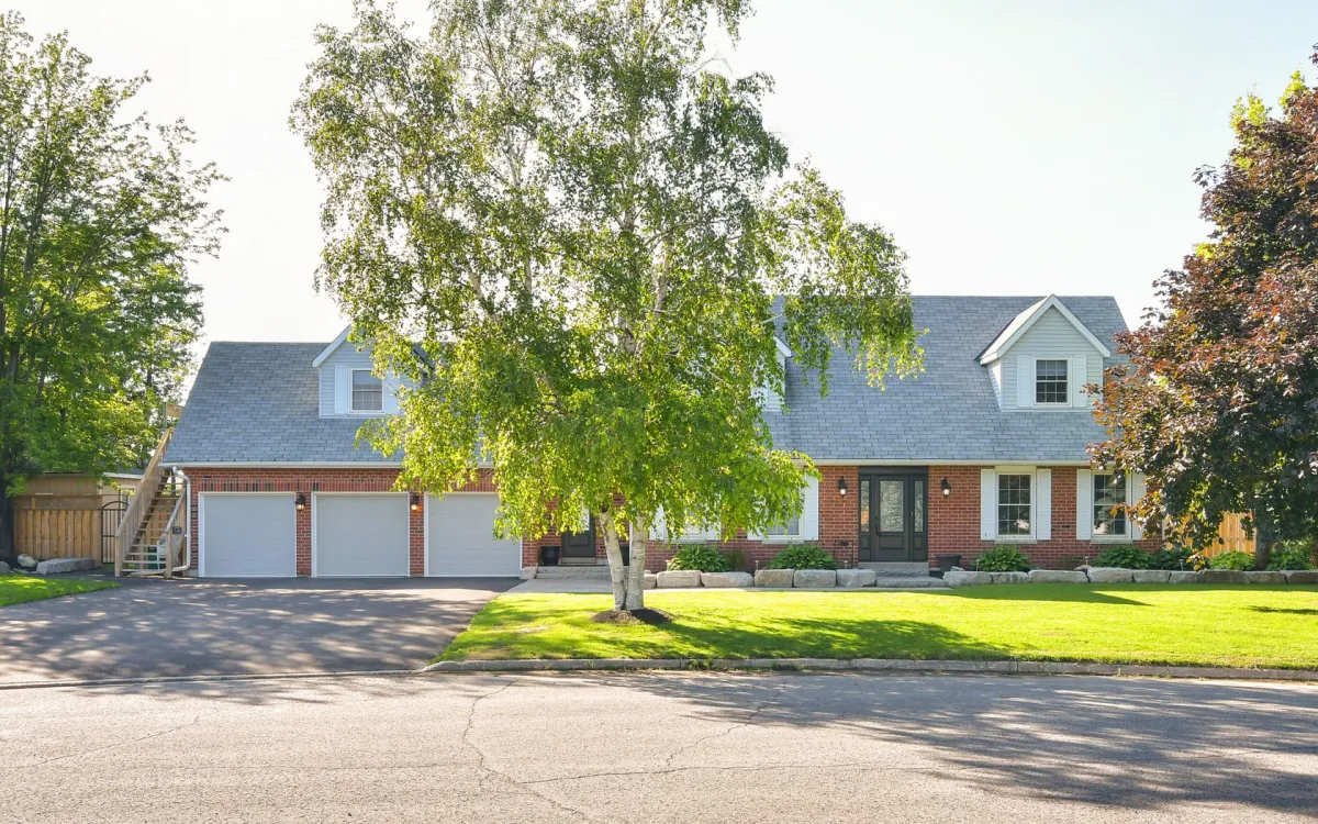 Two storey detached red brick home with attached 3-car garage with large lush lawn and mature tree located in the Park Lane neighbourhood in Orangeville