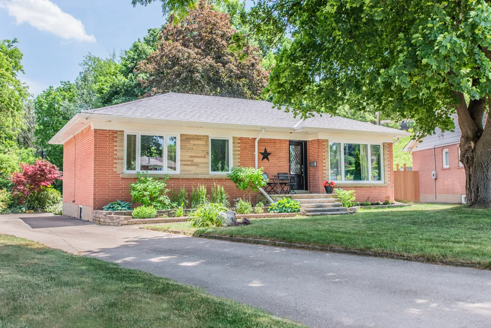 red brick bungalow style home with lush mature garden and trees with detached garage located in Halton Hills, Ontario
