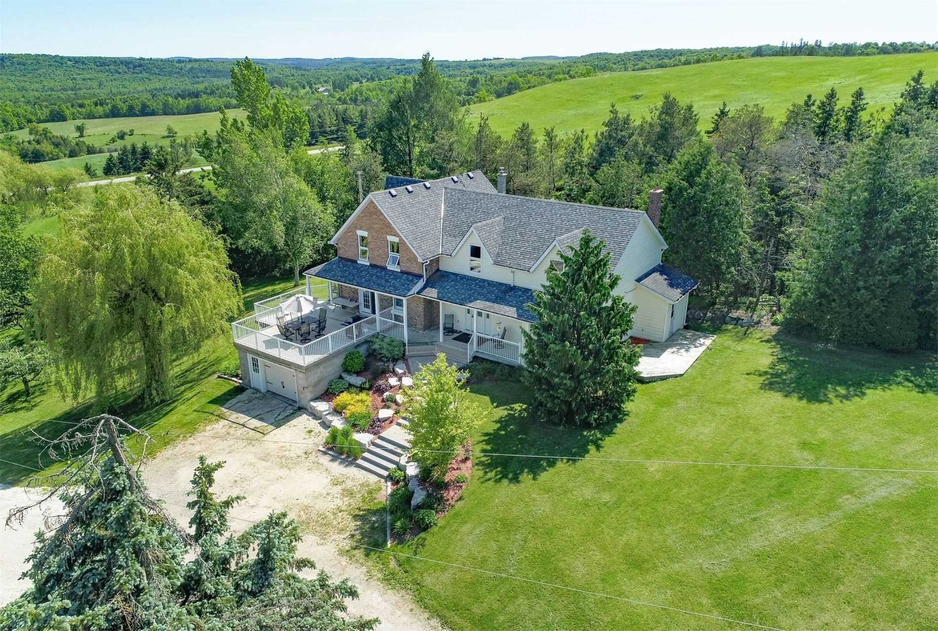 Large 2-storey farmhouse with raised porch surrounded by trees located in the Perm area of Mulmur Township