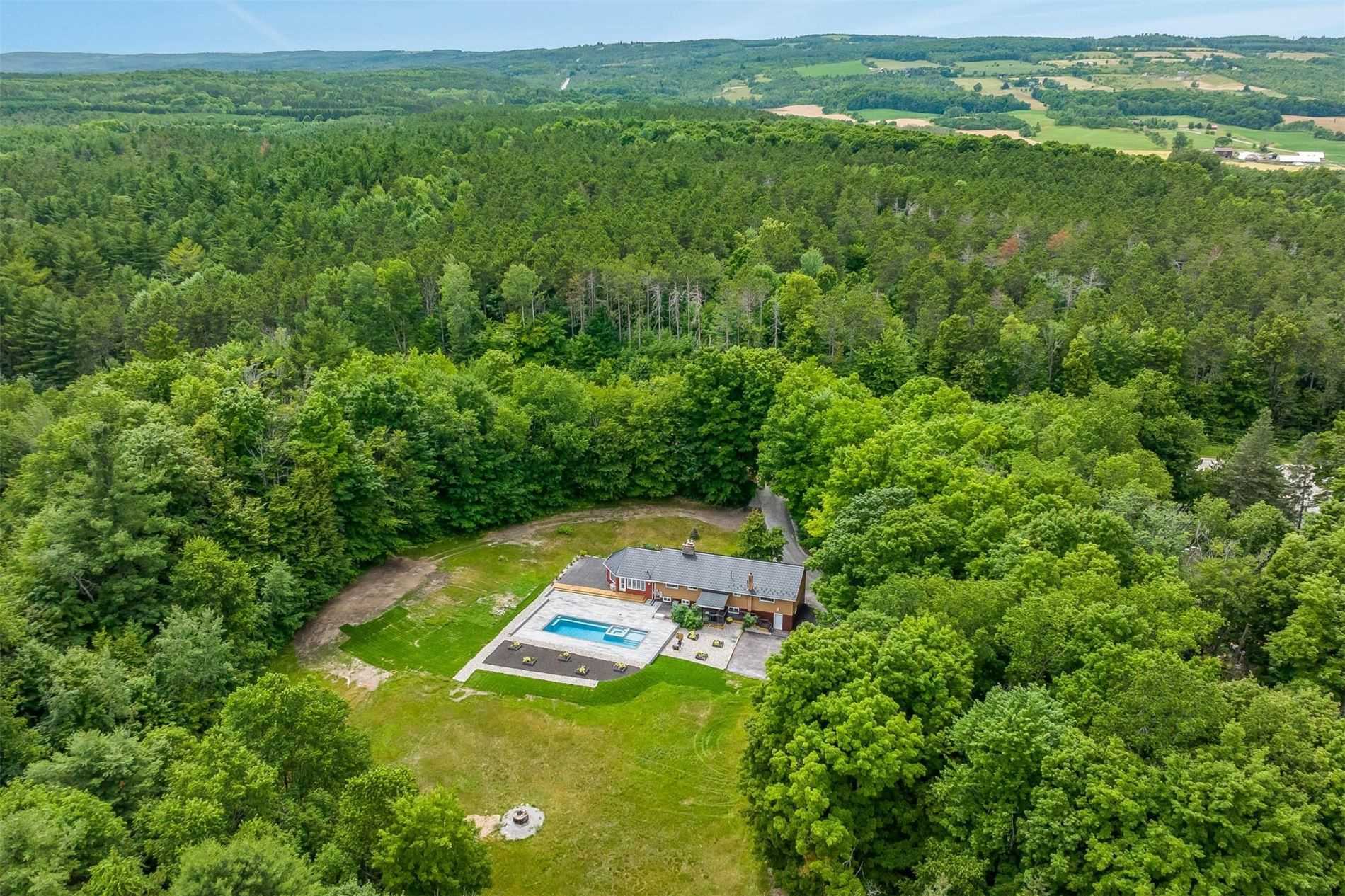 Aerial image showing a large property with bungalow and in-ground pool surrounded by trees located in the Randwick area of Mulmur Township